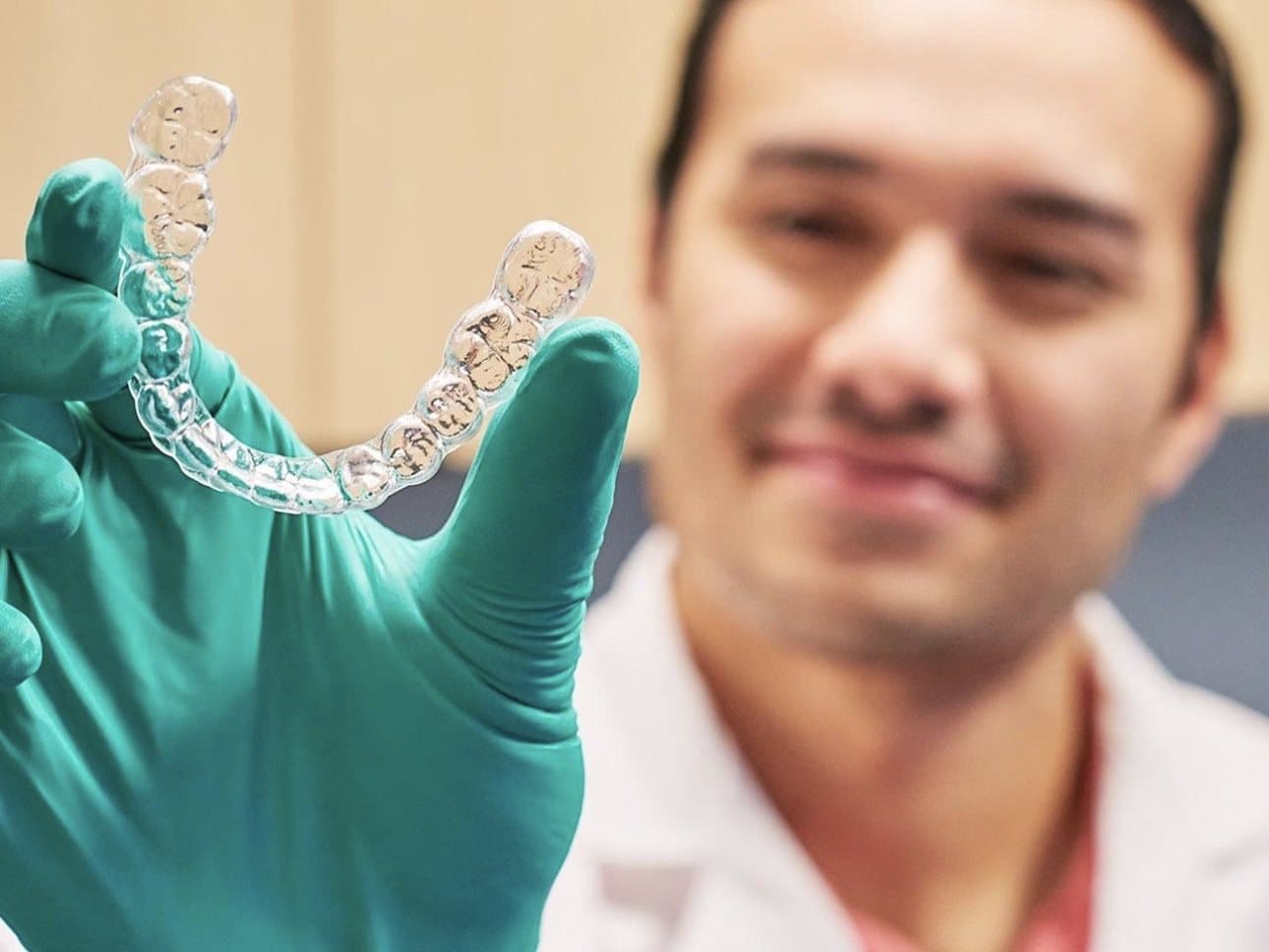 طبيب أسنان يحمل مصفّفة شفافة (Invisalign) بيد مرتدية قفّازًا طبّيًا أمام الكاميرا